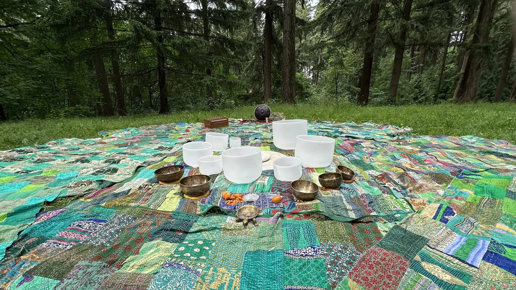 Crystal and Tibetan bowls on patchwork quilts in a clearing ringed by fir trees