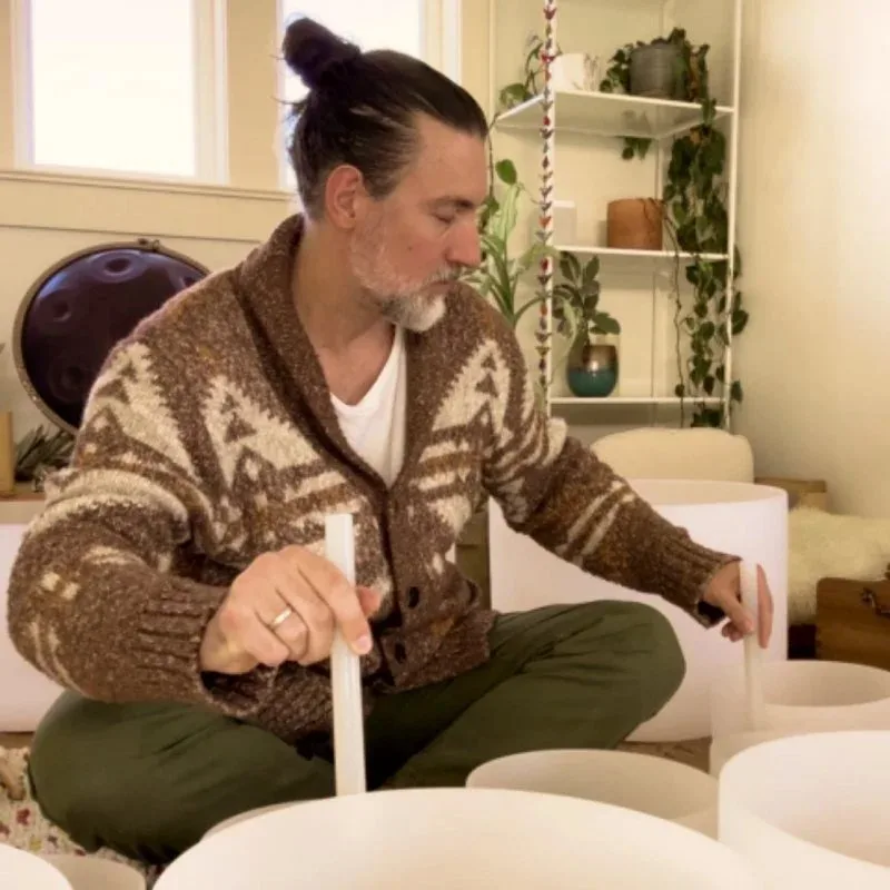 Graham Slick sitting cross-legged among crystal singing bowls, holding a striker